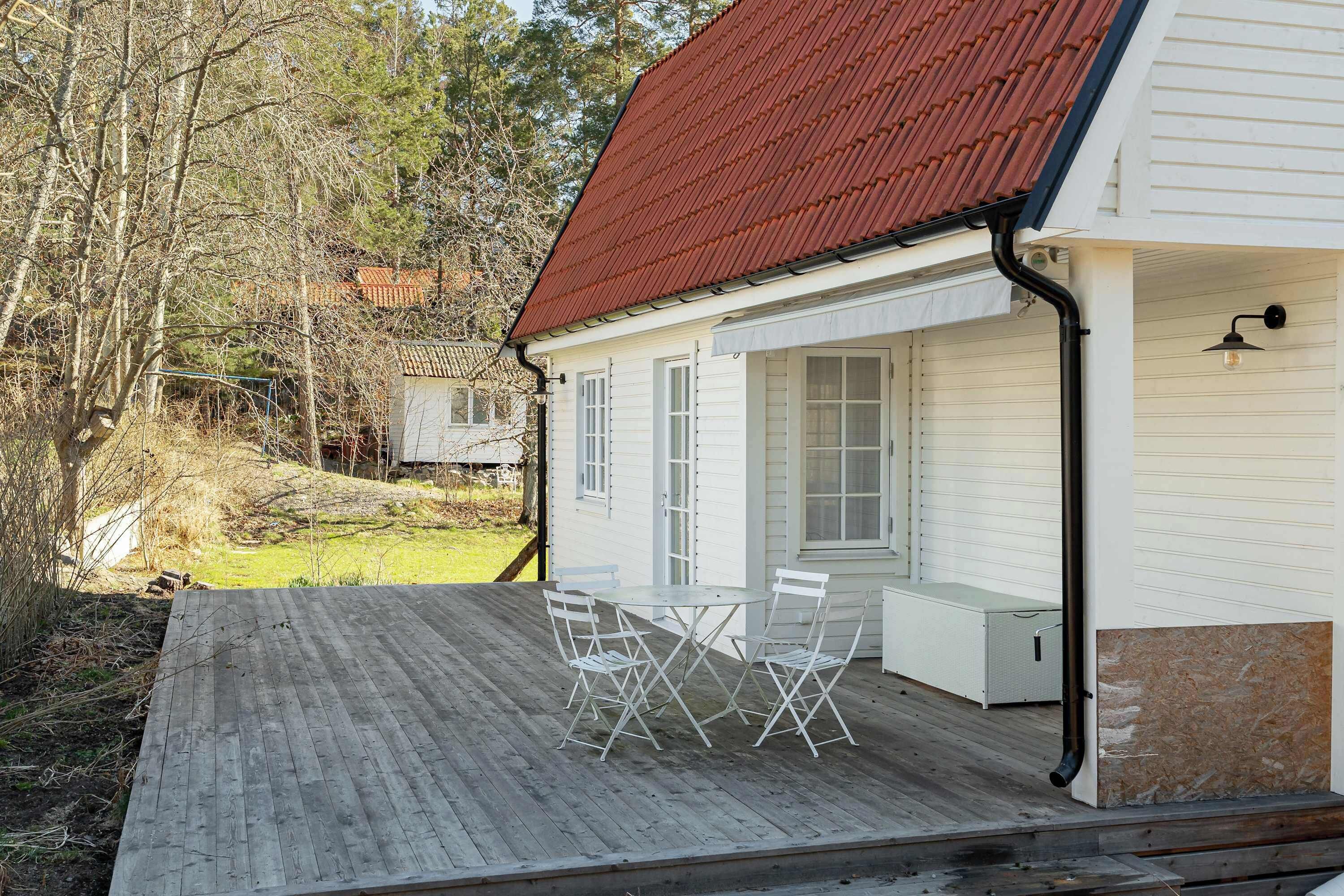 A white house with a red roof, a wooden deck, and a table with chairs.
