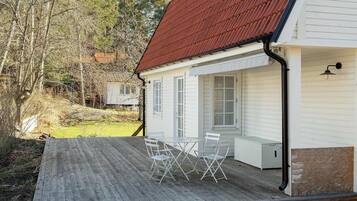 A white house with a red roof, a wooden deck, and a table with chairs.