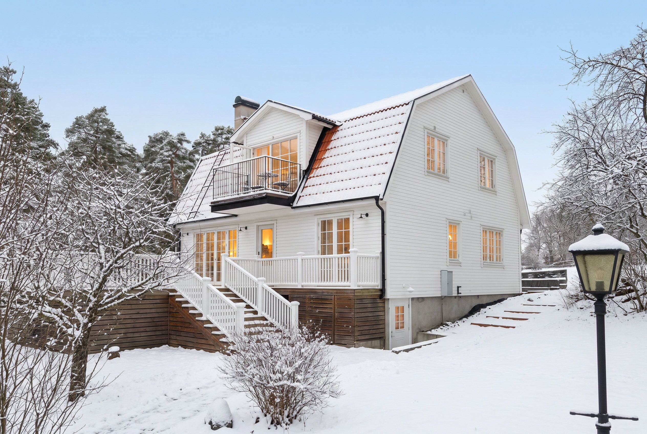 Ett tvåvåningshus med en balkong, en trappa som leder upp till entrén och ett snötäckt landskap.
