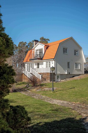 Una casa a due piani con facciata bianca, tetto arancione e una scala in legno che conduce a un balcone.
