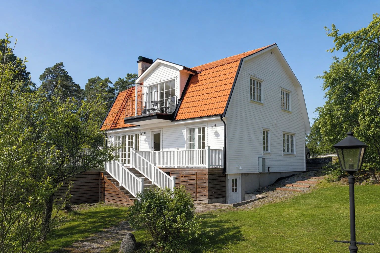 Ett tvåvåningshus med ett rött tegeltak, vita ytterväggar och en veranda med en trappa.
