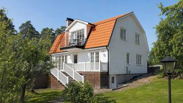 Ett tvåvåningshus med ett rött tegeltak, vita ytterväggar och en veranda med en trappa.