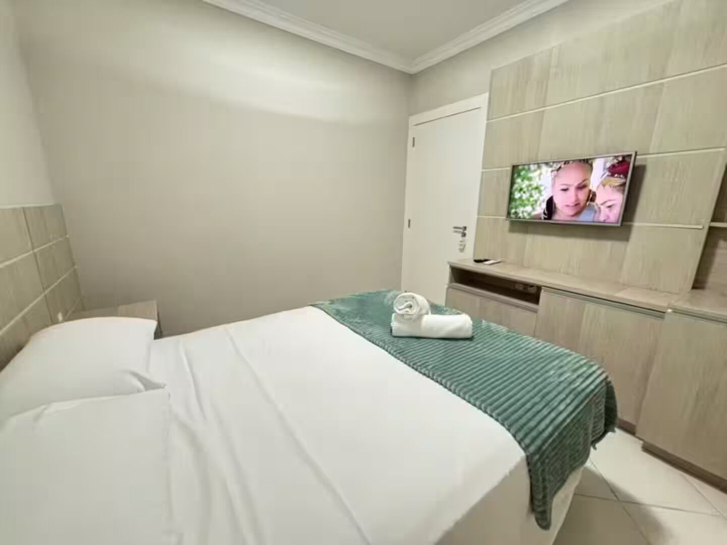 A hotel room with a bed, a television mounted on the wall, and a small desk area.