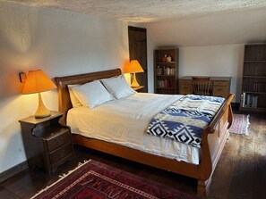 Un dormitorio con una cama de madera, dos mesitas de noche, una mesita auxiliar, una estantería y un escritorio.