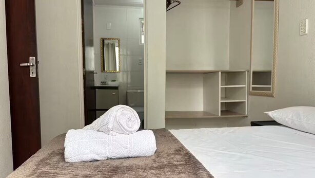 Een hotelkamer met een bed, een zichtbare badkamer door een open deur, en een inloopkast met planken.