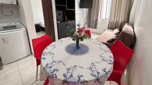 Een eetgedeelte met een ronde tafel, stoelen, een plafondventilator, een televisie en een bed met gordijnen.