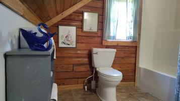 A wooden-paneled bathroom with a toilet, a framed picture, and a blue glass vase on a cabinet.