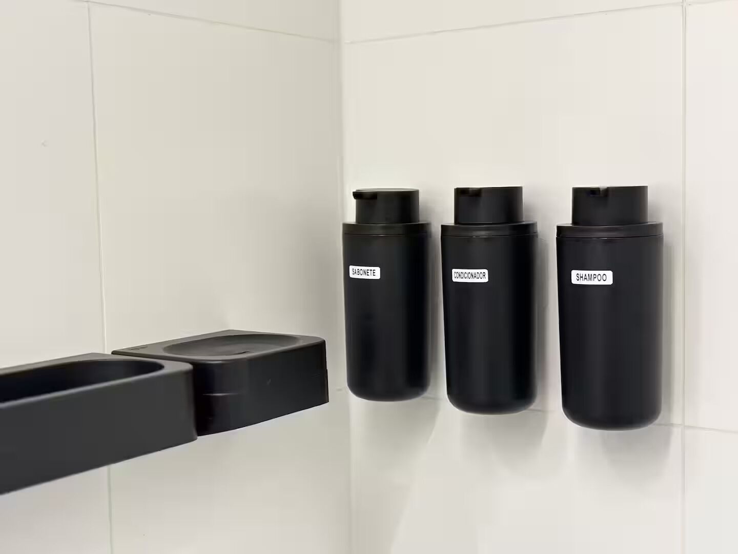 A bathroom with a black soap dispenser, a black shampoo bottle, and a black conditioner bottle mounted on the wall.