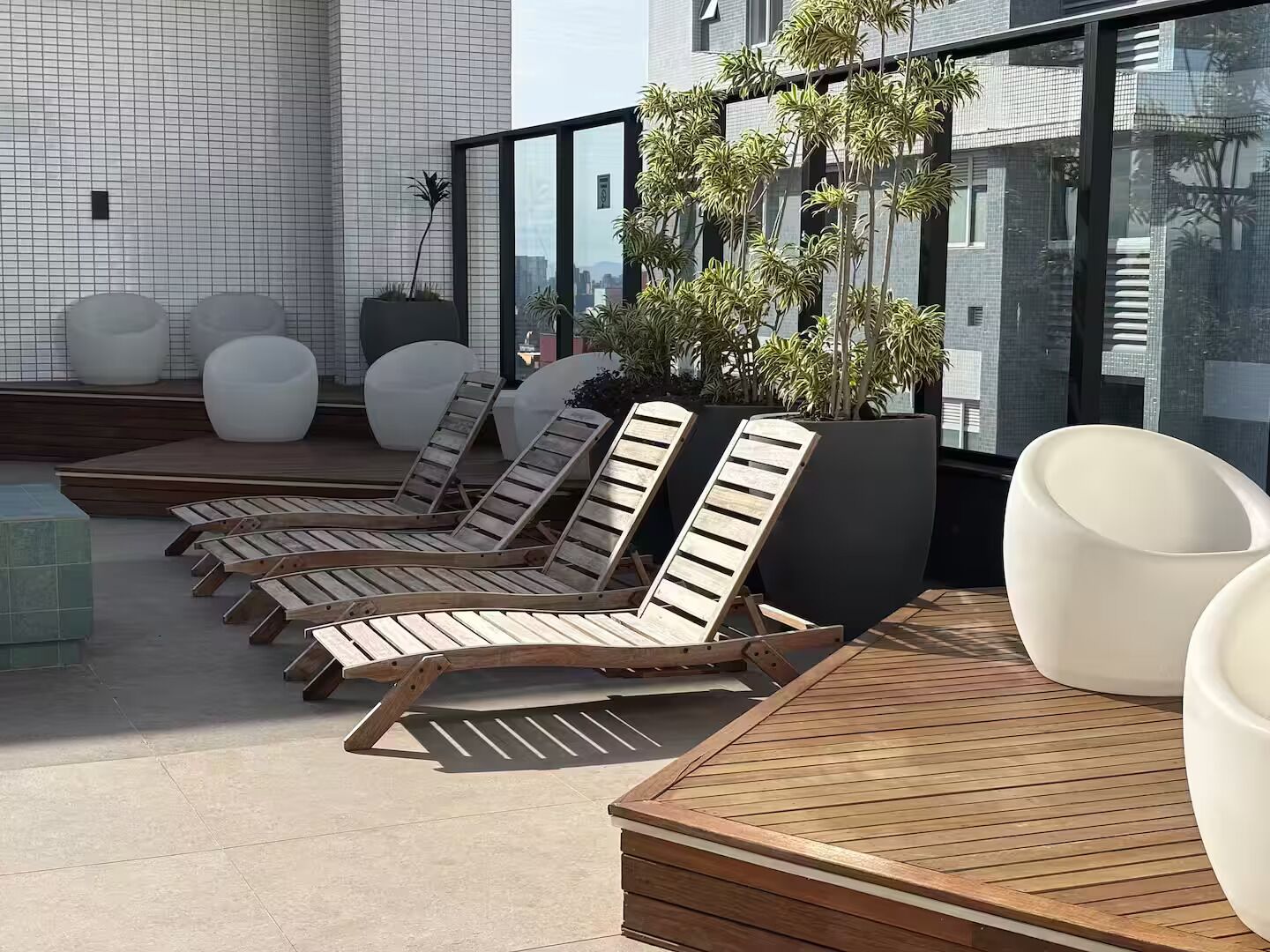 A rooftop lounge area with wooden loungers, potted plants, and a view of the city.
