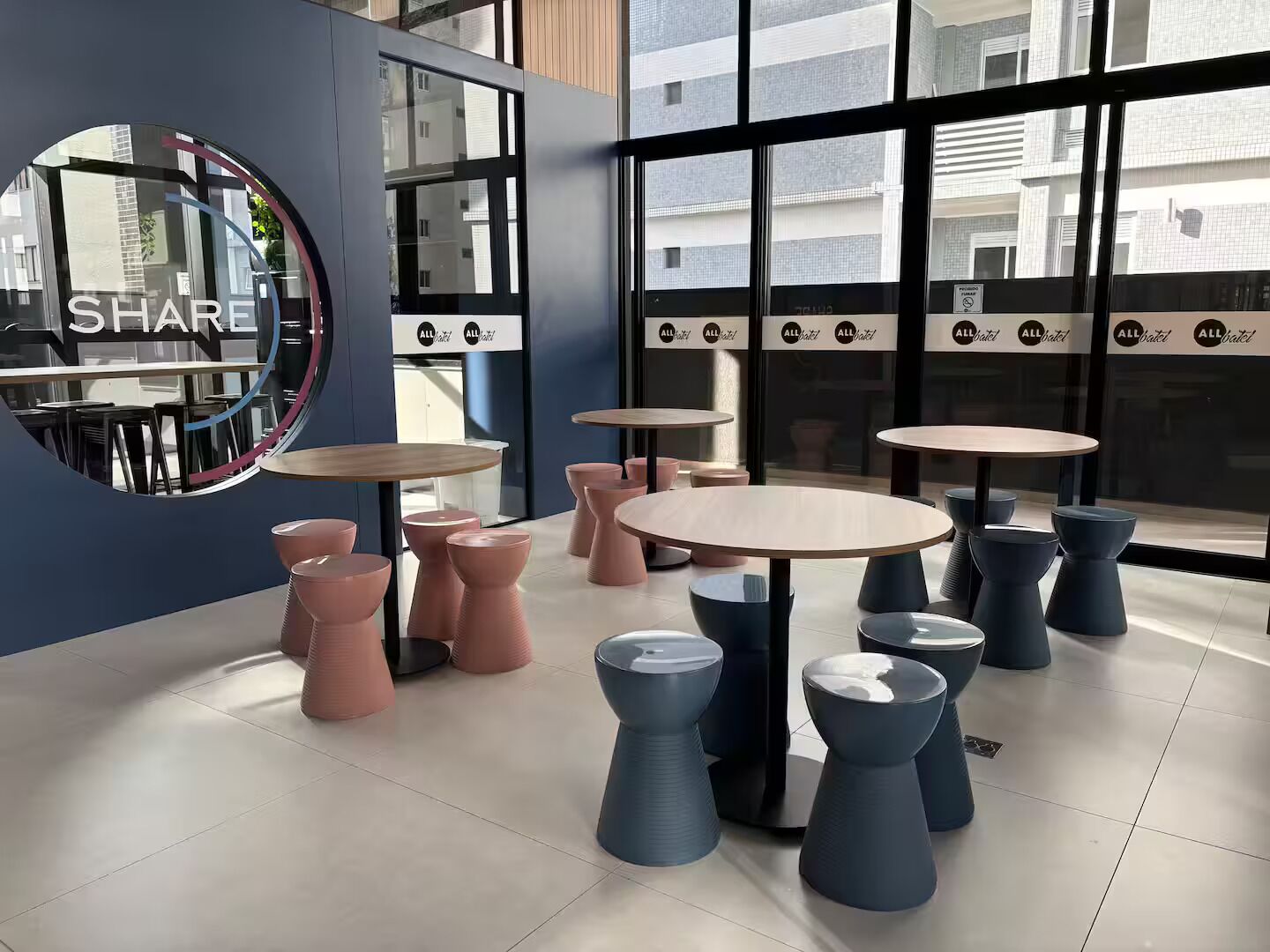 A modern interior with round tables and stools, large windows, and a 'SHARE' sign on the wall.