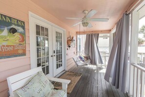 Une véranda avec une balançoire, un banc, un ventilateur de plafond et une porte à panneaux de verre.