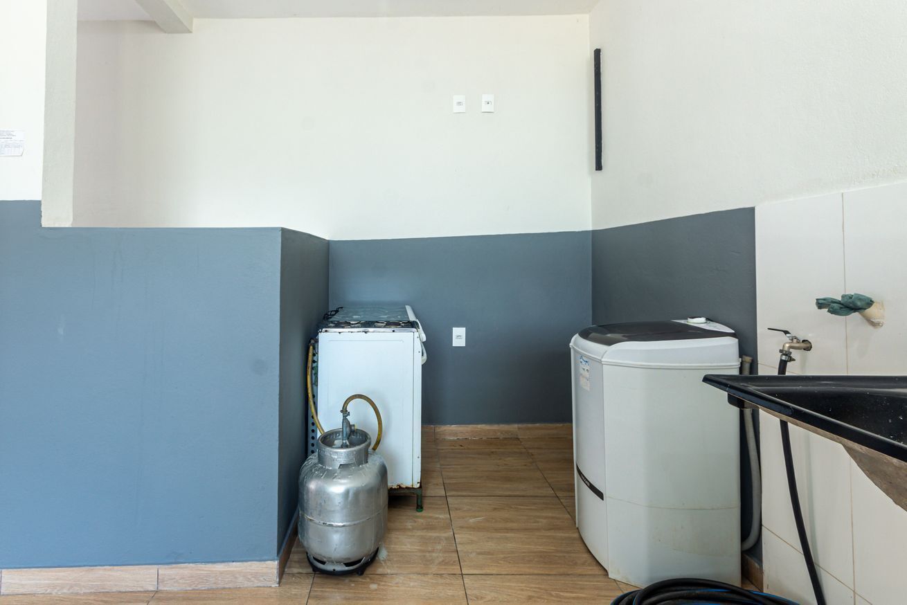 A compact kitchen with a refrigerator, a washing machine, and a gas cylinder.