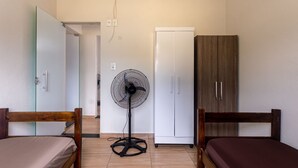 A bedroom with two wooden beds, a white wardrobe, a glass door, a standing fan, and a white ceiling fan.