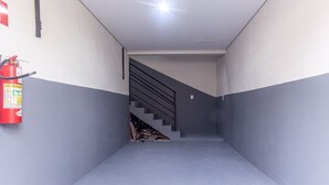 A narrow hallway with a fire extinguisher on the left, a staircase in the center, and a plain wall on the right.