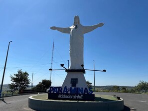 A statue with outstretched arms, a pedestal with inscriptions, and a circular base. - Apartamento 4 Quartos com Wi-fi e Garagem (Para de Minas)