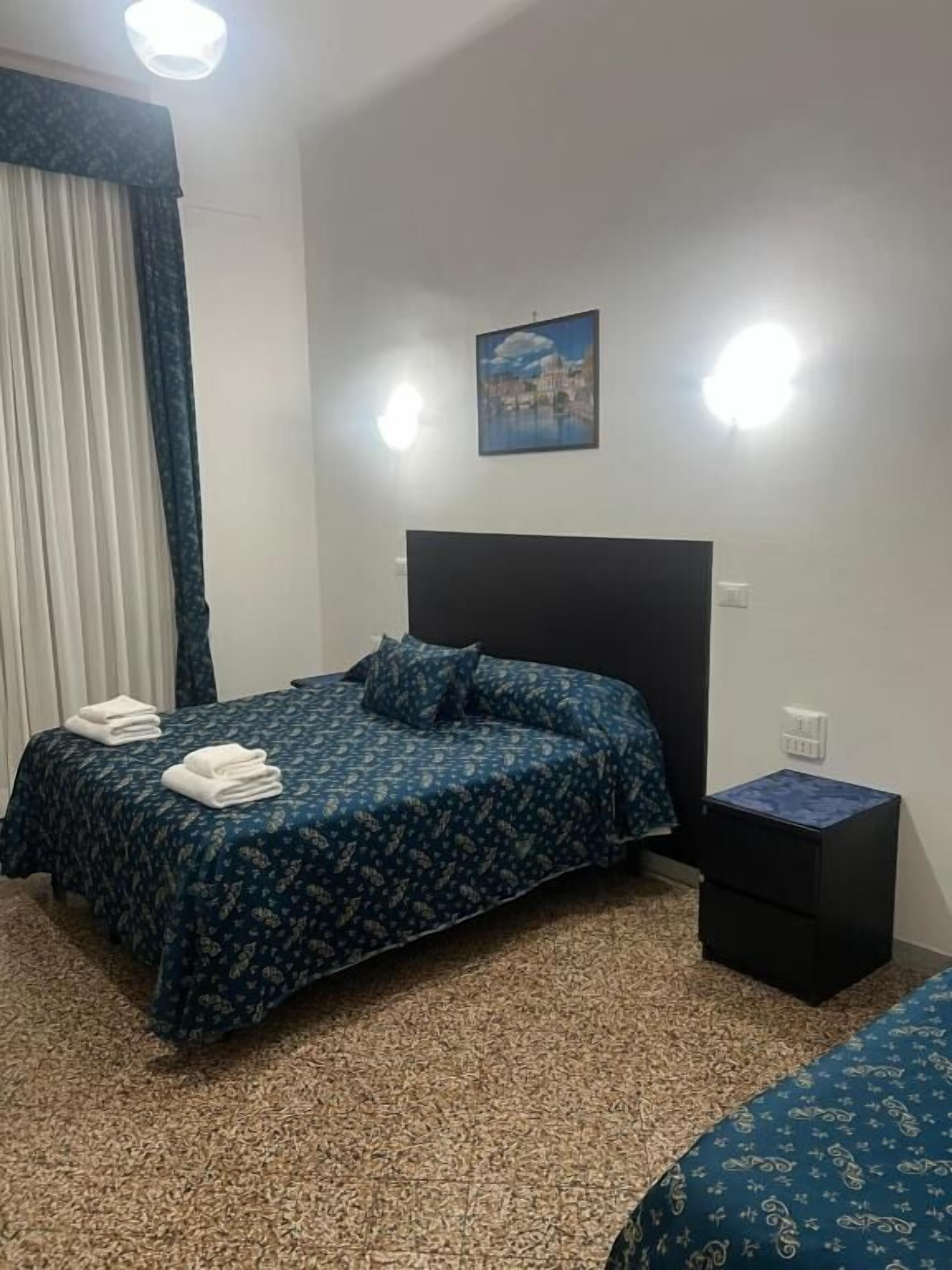 A bedroom with a bed, a nightstand, a wall-mounted light, and a painting.