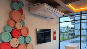 A modern interior with a wall-mounted TV, a fire extinguisher, and a large window with a view of the outdoors. - Cais Eco Residencia by Manta e BHL (Ipojuca)