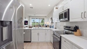 A modern kitchen with stainless steel appliances, white cabinetry, and a view to the outdoors. - #321 - Luxury - Golf Course Views - Sleeps 6 (Naples)