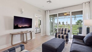 A living room with a flat-screen TV, a wooden coffee table, a sofa, and a balcony with a view of a golf course. - #321 - Luxury - Golf Course Views - Sleeps 6 (Naples)