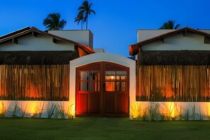 A modern building with a central entrance, flanked by two structures with thatched roofs and vertical wooden slats.