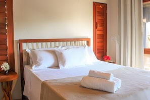 A hotel room with a wooden headboard, a bed with white linens, a small table with a vase of flowers, and a window with curtains.