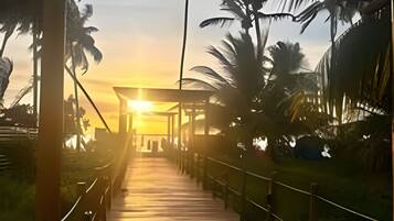 A wooden boardwalk leading to a structure with a roof, surrounded by palm trees.