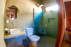 Casa de banho com sanita, lavatório, espelho e cabine de duche em vidro.