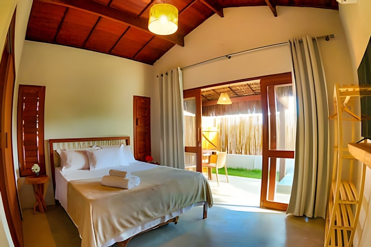 Quarto com uma cama, mesa de cabeceira, abajur e vista para o exterior.
