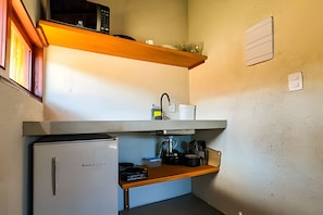 Una kitchenette compacta con refrigerador, microondas, pileta y estante con utensilios de cocina.