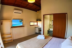 A bedroom with a bed, a television on a shelf, a desk with a computer, a mirror, and an air conditioning unit.
