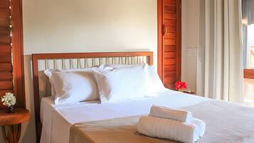 A hotel room with a wooden headboard, a bed with white linens, a small table with a vase of flowers, and a window with curtains.