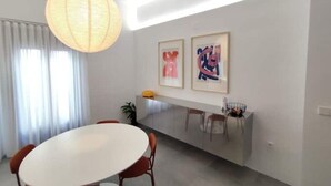 Un espace de salle à manger moderne avec une table ronde, des chaises, un luminaire suspendu et deux œuvres d’art encadrées accrochées au mur.