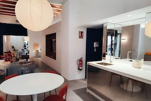 Eine moderne Hotellobby mit einem runden Esstisch, roten Stühlen, einer großen Hängeleuchte, einem Feuerlöscher und einer Spiegelwand.