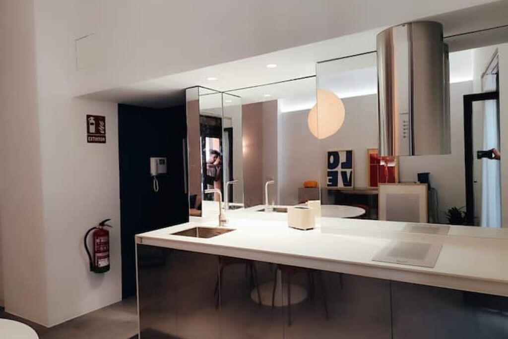 A modern kitchen with a large island, a fire extinguisher, and a mirror.
