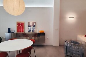 Un espace repas moderne avec une table ronde, des chaises rouges, un luminaire suspendu et un coin cuisine doté d’un meuble rouge et d’un plan de travail blanc.