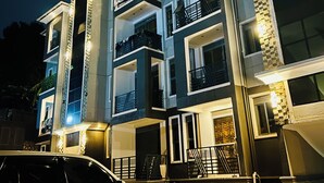 Um edifício com várias andares, varandas, um carro estacionado em frente e fachada de tijolos.