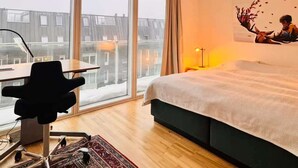 Ein Hotelzimmer mit großem Fenster, einem Bett, einem Schreibtisch mit Stuhl und einem Teppich.
