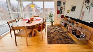 Ein modernes Wohnzimmer mit Esstisch aus Holz, Stühlen, einer Couch und einem Bücherregal.