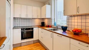 Eine moderne Küche mit weißen Schränken, einer Holzarbeitsplatte, einem eingebauten Backofen und einem Fenster mit Blick auf die Stadt.