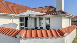 A house with a red-tiled roof, a white exterior, and a covered patio with a table and chairs. - Beautiful home in Blokhus with WiFi (Blokhus)