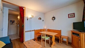 Ein gemütliches Wohnzimmer mit einer hölzernen Bank, einem kleinen Tisch, einem Fernseher auf einem Holzschrank und einer Tür, die in einen anderen Raum führt.
