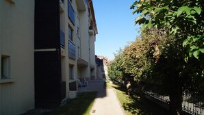 En smal gångväg mellan byggnaderna, ett staket som kantas av träd och en klar himmel.