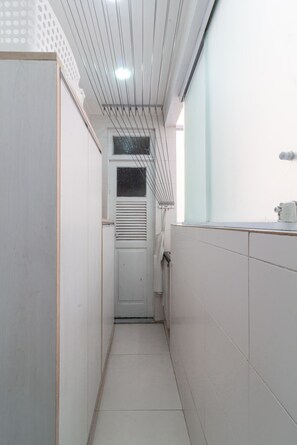 A narrow hallway with white tiled walls, a door at the end, and a window with blinds. - 10-min Walk to Copacabana Beach | STC302 (Rio de Janeiro)