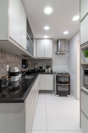 A modern kitchen with white cabinets, a black countertop, a built-in oven, and a stainless steel range hood. - 10-min Walk to Copacabana Beach | STC302 (Rio de Janeiro)