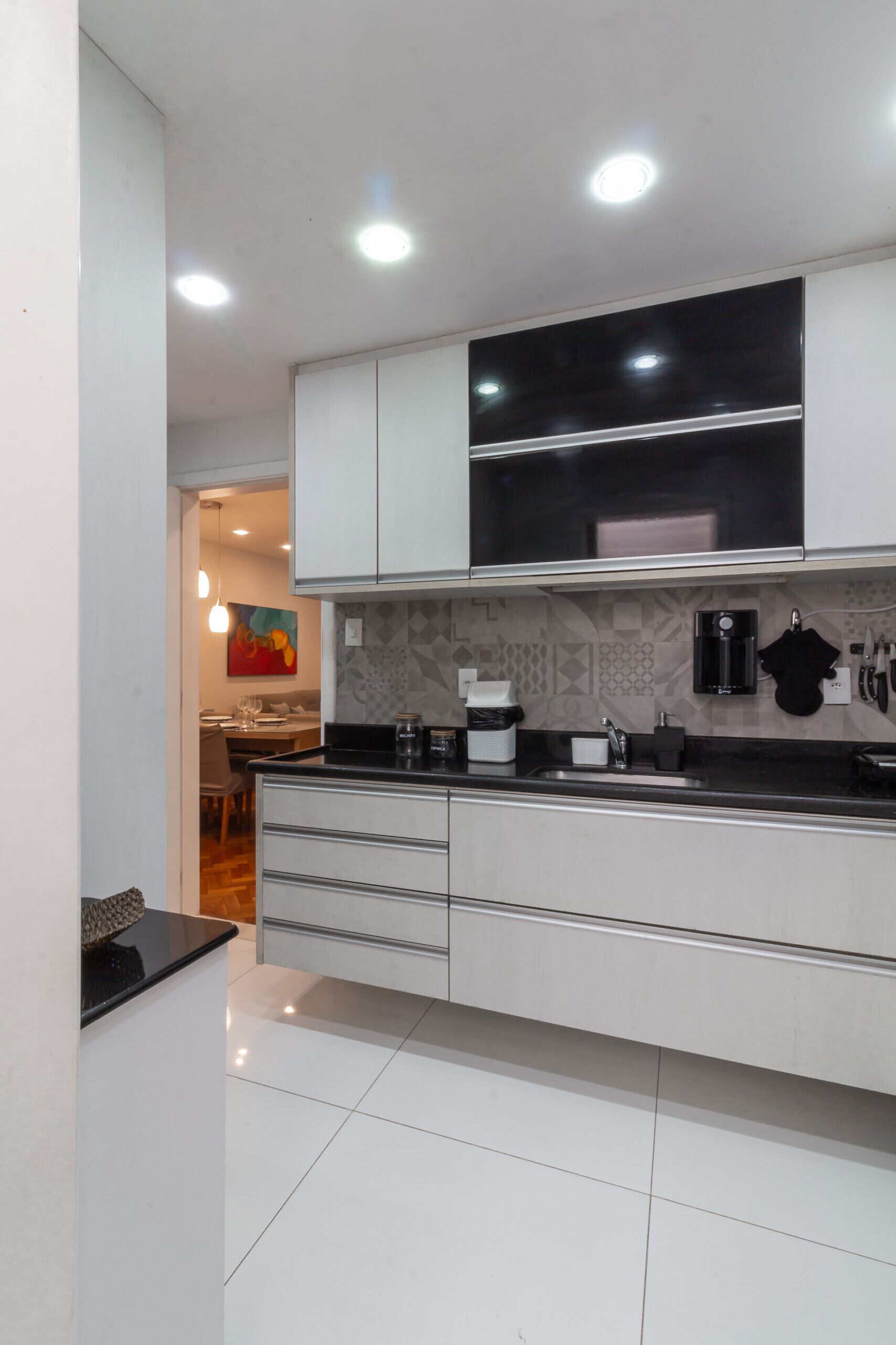 A modern kitchen with white cabinets, a black countertop, and a coffee machine.