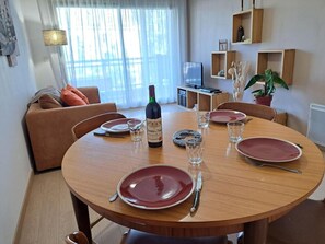 Ein Essbereich mit einem runden Holztisch, gedeckt für vier Personen, einer Weinflasche und einem Fernseher im Hintergrund.