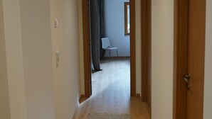 Un pasillo con suelo de madera, una zona alfombrada y una puerta que da a un cuarto con una silla y un ventanal.