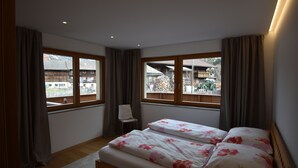 Un dormitorio con una cama, una silla y ventanas amplias que ofrecen vistas a edificios y un tractor afuera.