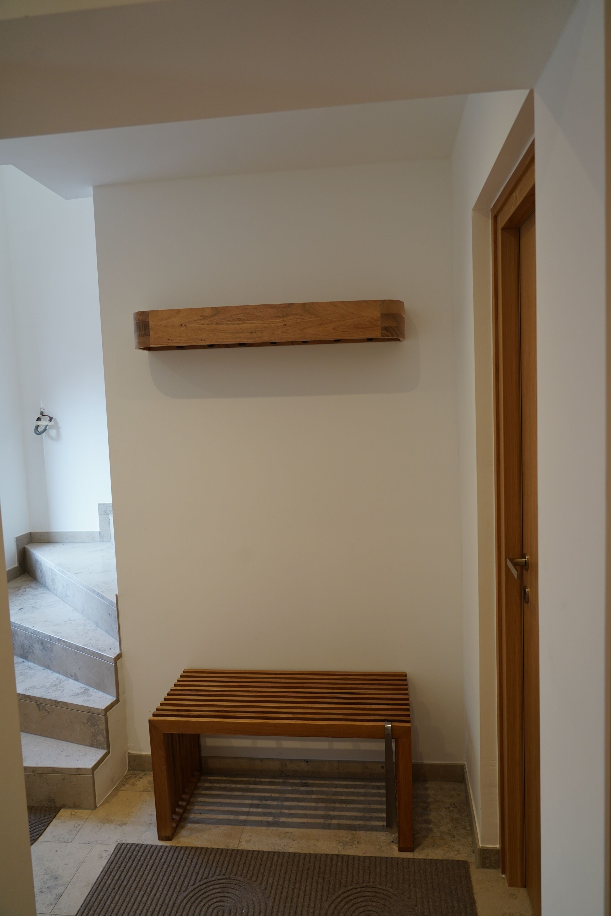 Un couloir avec un banc en bois, une étagère en bois et une porte.