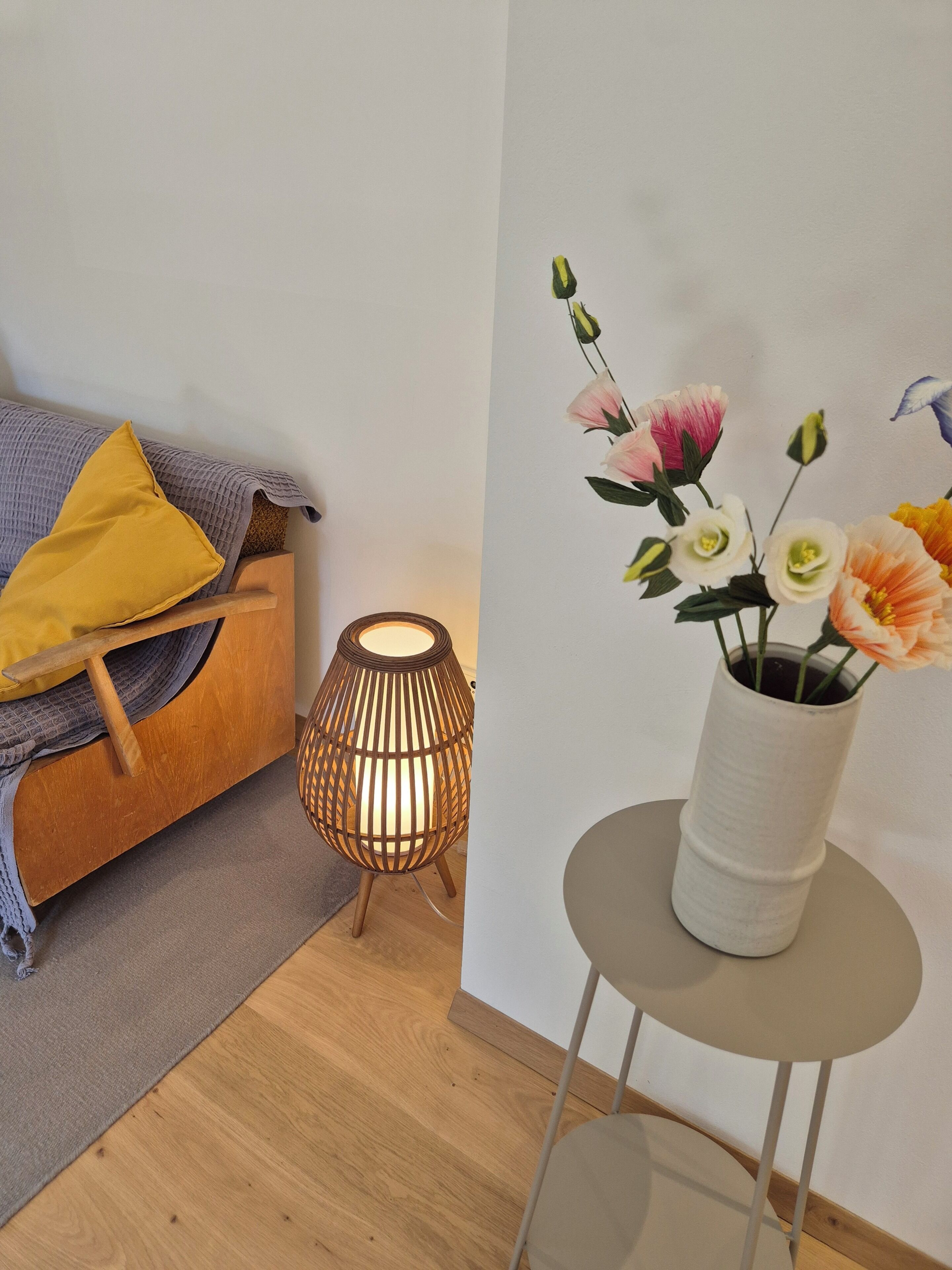 Une pièce avec un canapé en bois, une petite table sur laquelle est posé un vase de fleurs et un lampadaire.